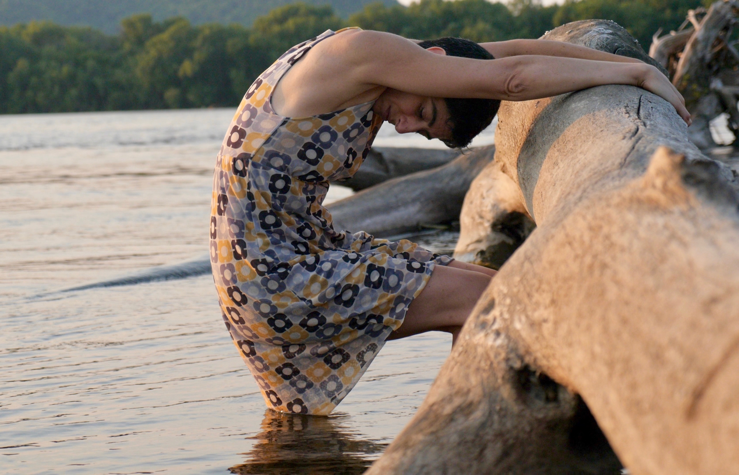 Dancer holding onto driftwood on the shore of a lake