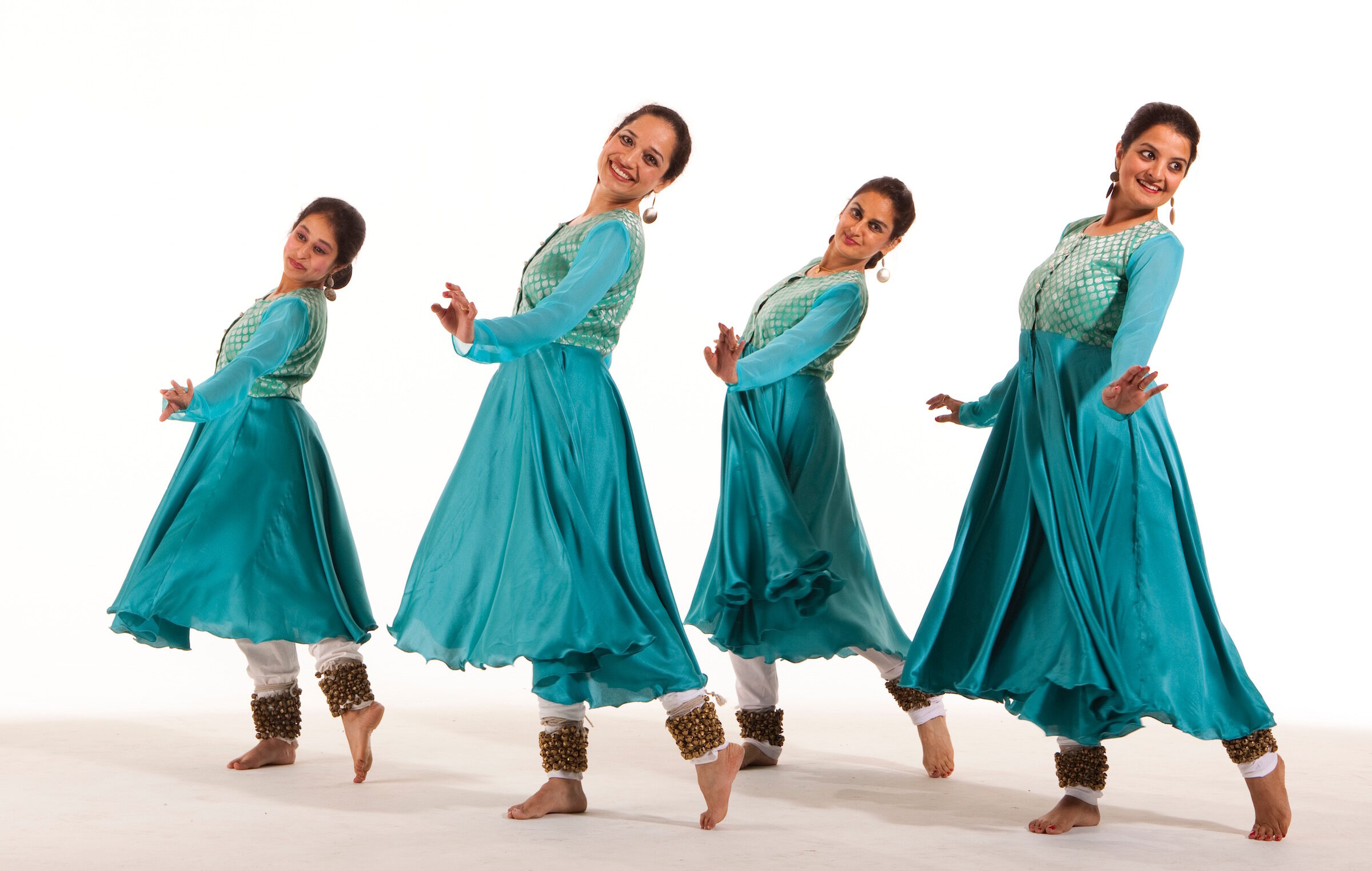 Four dancers in teal dresses looking over their shoulders