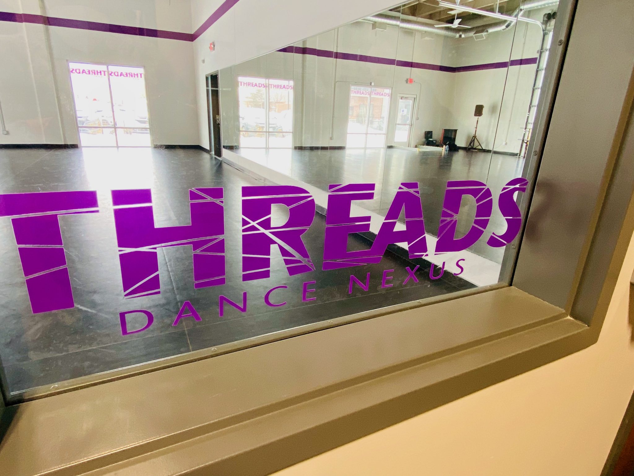 Photo looking through a window into the Threads Nexus Studio. The Threads logo is impressed on the glass of the window.