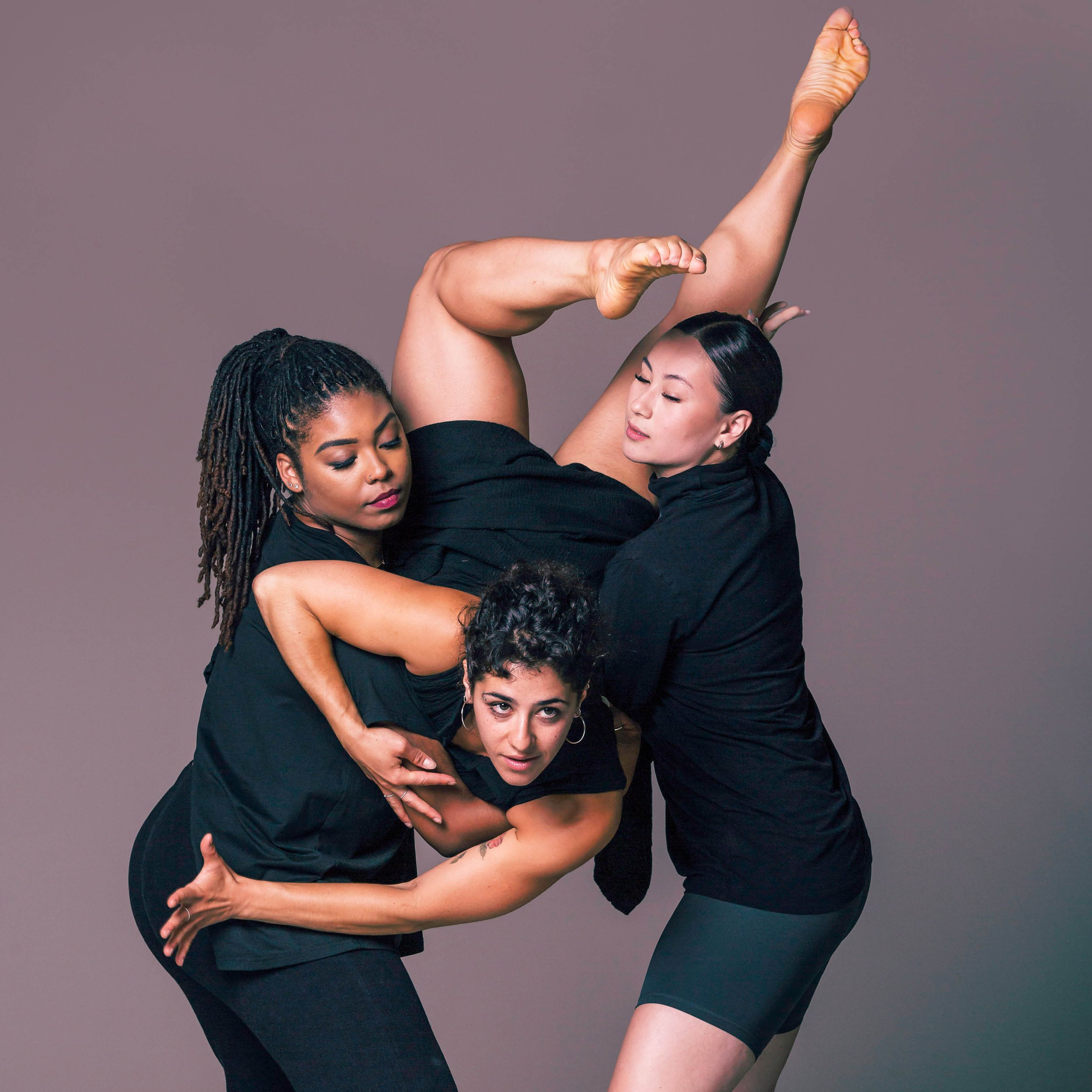 Two dancers suspend a third dancer leaping toward the camera