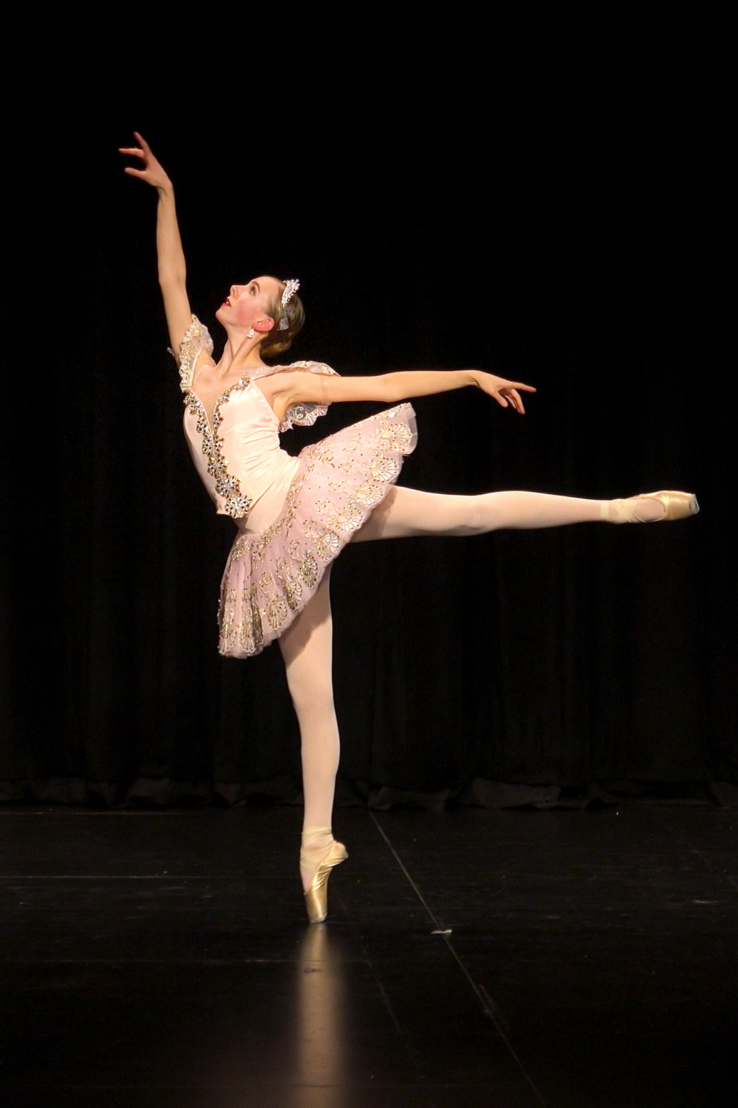 A light-skinned ballerina performs an arabesque en pointe dressed as the Sugar Plum Fairy