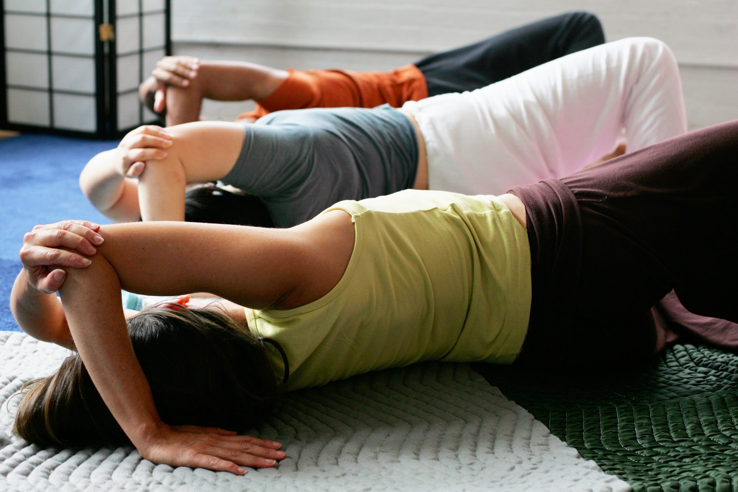 three people lay on the floor with one arm over their head, elbow bent, and hand on the floor