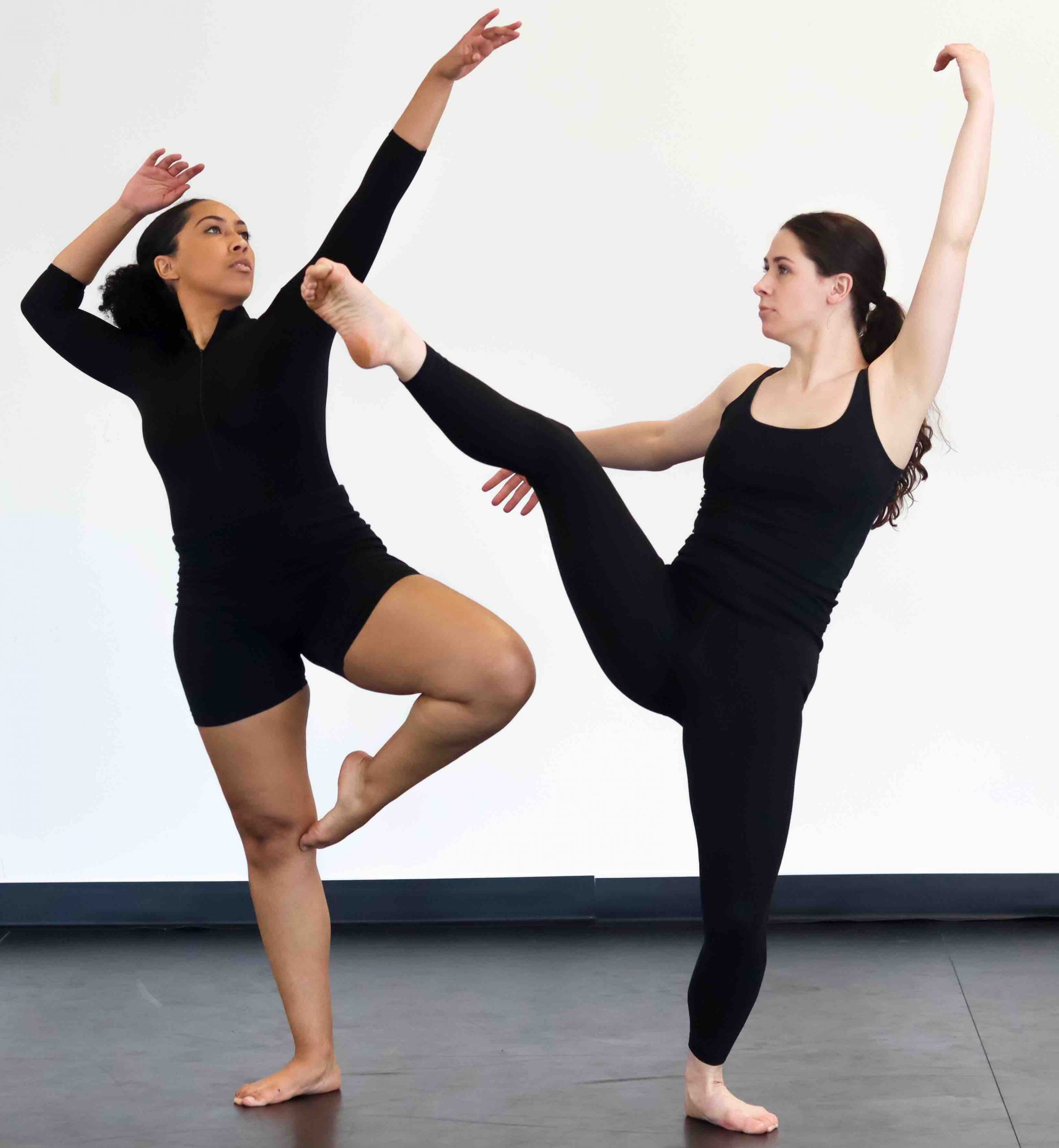 A dark-skinned dancer stands in passe and a light skinned dancer stands in front attitude