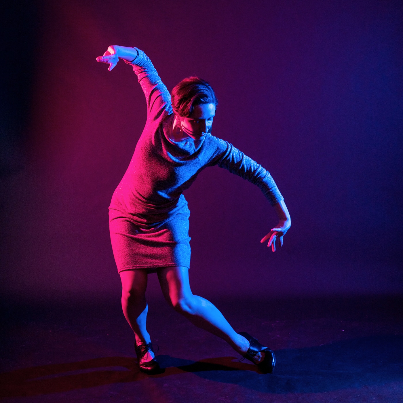 A light skinned flamenco dancer poses in dramatic, colorful lighting