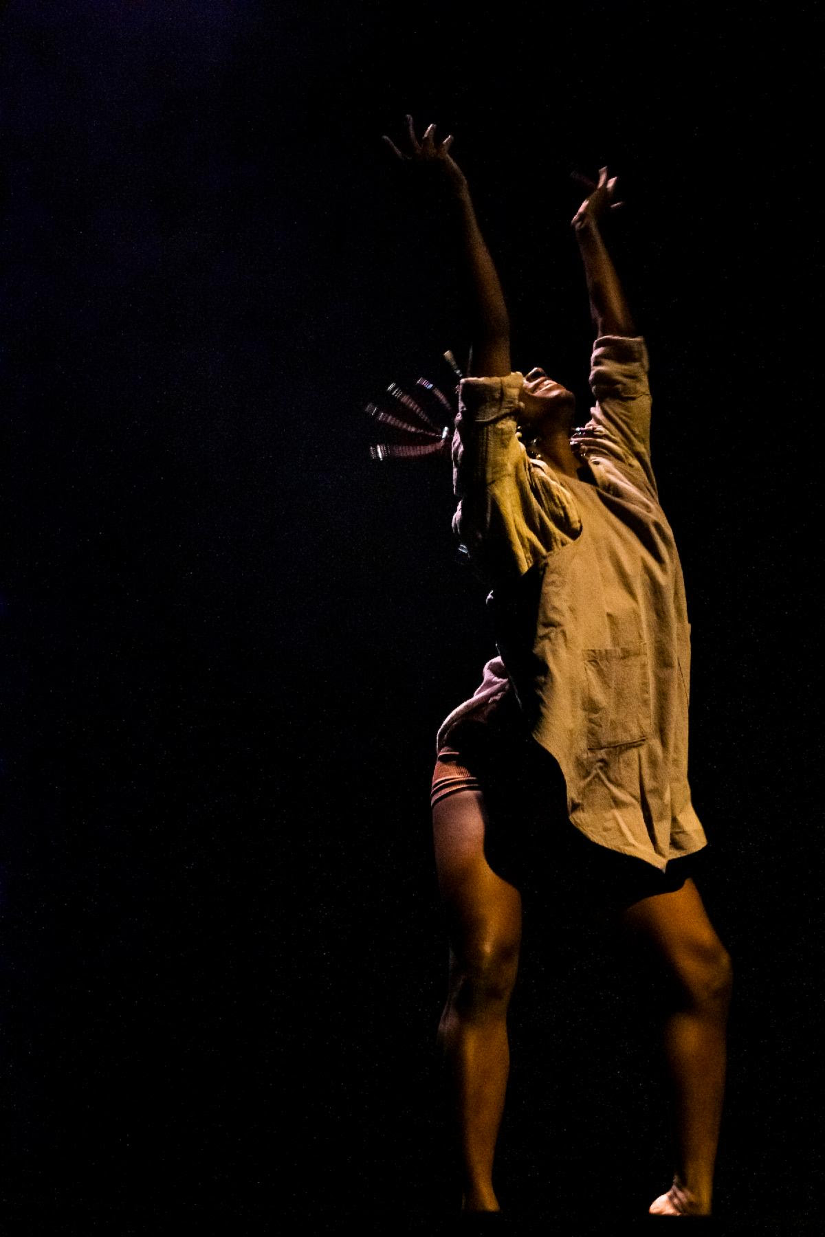 Alanna Morris, a black dancer, is on stage in a beige button-up shirt, as she arches her back and gazes toward the ceiling