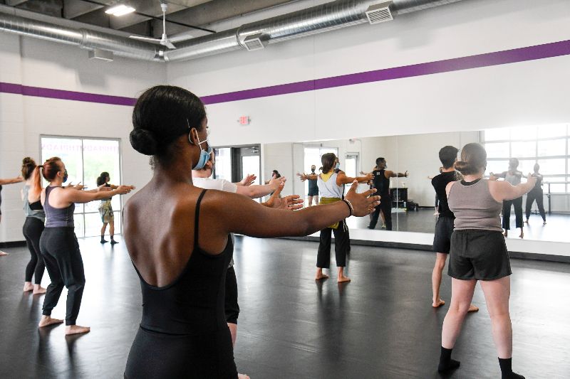 A photo of a community class at the Threads Dance Nexus. Several adults of varying skin tones stand in parallel position with arms reaching forward
